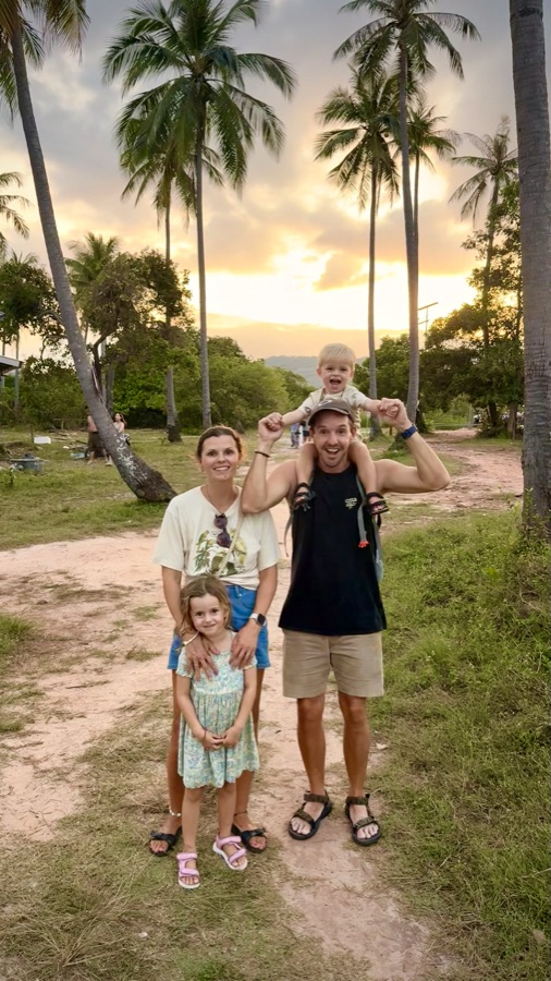 Familie auf einem Palmenweg bei Sonnenuntergang